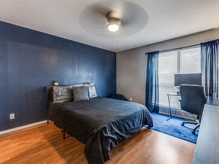 Room featuring wood-finish flooring, a ceiling fan with integrated lighting, and a prominent blue accent wall