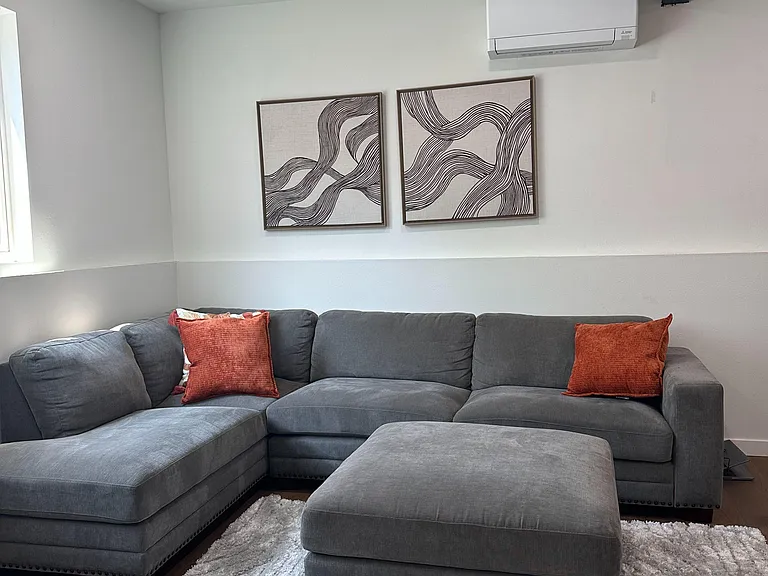 Spacious living area with a large sectional, ottoman, and area rug, plus recessed lighting and a wall-mounted mini-split.
