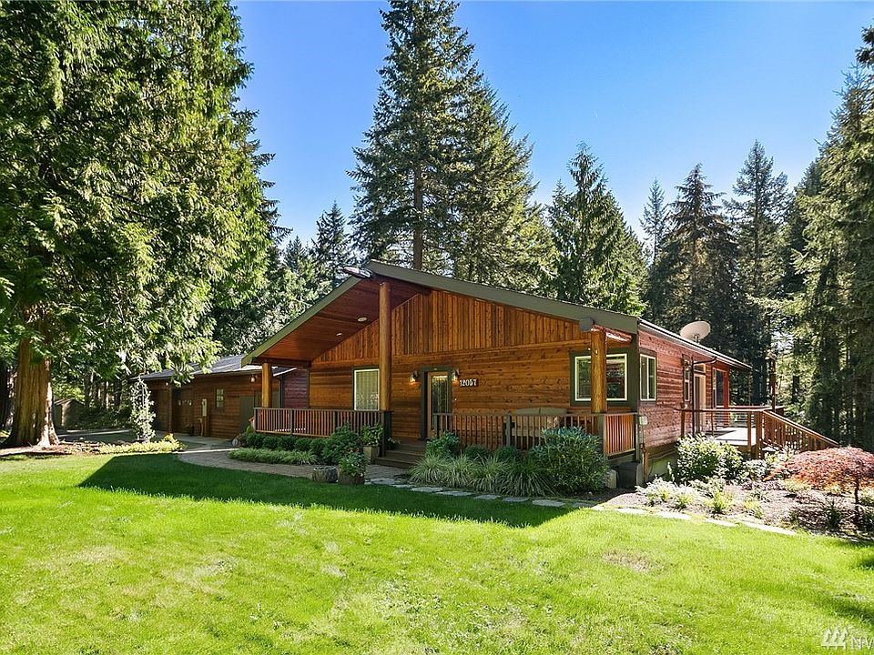 This home welcomes you in with its enveloping entry deck and generous lawn. This photo is taken from near to  the north west corner as you arrive. Garage with shop space is on the left.
