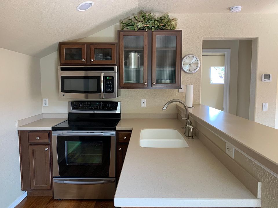 Kitchen fully loaded with range oven, microwave, refrigerator, laundry washer/dryer combo, and countertop dishwasher.