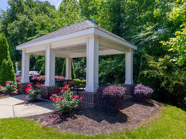 Landscaped outdoor pavilion with brick accents, picnic seating, and flower beds, offering shaded relaxation at Snowden Senior Apartments.