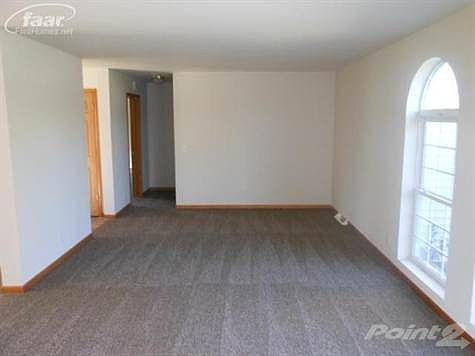 Large open living room with fresh paint, carpet and dual arched windows overlooking the front yard.