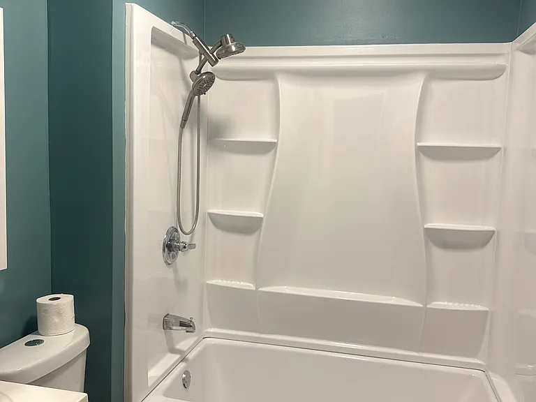 Modern bathroom featuring a full-size tub/shower combo with built-in shelving, updated fixtures, a bright vanity, fresh paint, and a clean, contemporary design. Spacious, low-maintenance, and perfect for everyday comfort