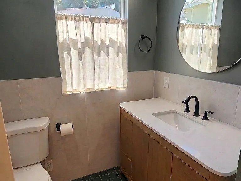 Downstairs bathroom with single vanity, custom tile, and glazed lower window with cafe curtain for privacy.
