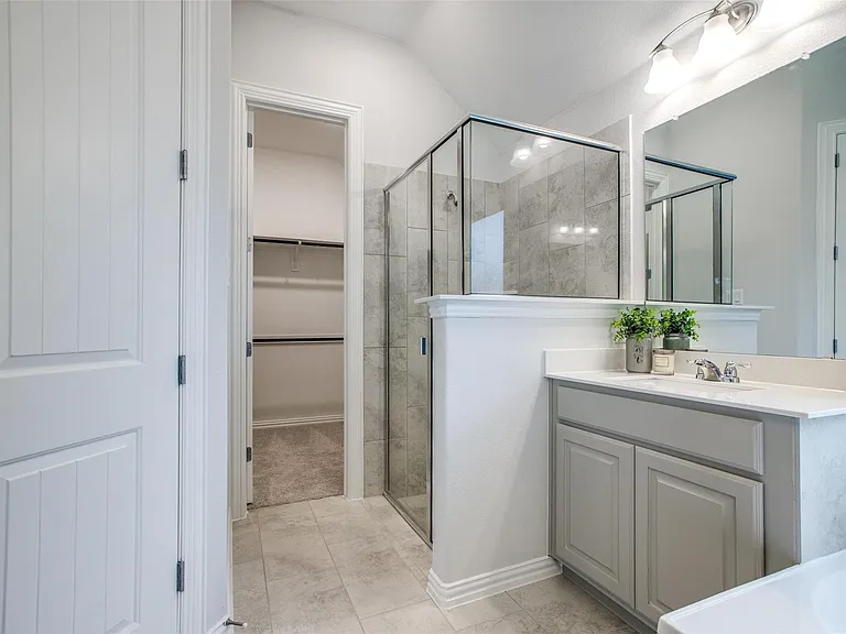 Bathroom featuring a glass-enclosed shower with tile surround, a single vanity with stone countertop, and tile flooring