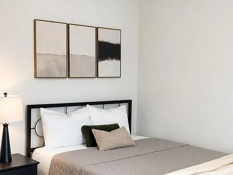 Private bedroom with a full-size bed, nightstand with lamp, and clean neutral walls with simple artwork.