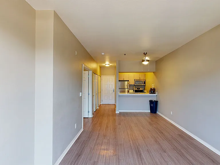 Apartment kitchen with stainless steel appliances, dining and living room with wood-style flooring.