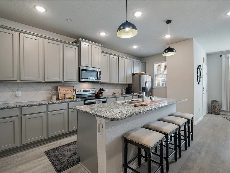 Kitchen featuring an island with seating, stainless steel appliances, light gray cabinetry, mottled countertops, and wood-finish flooring