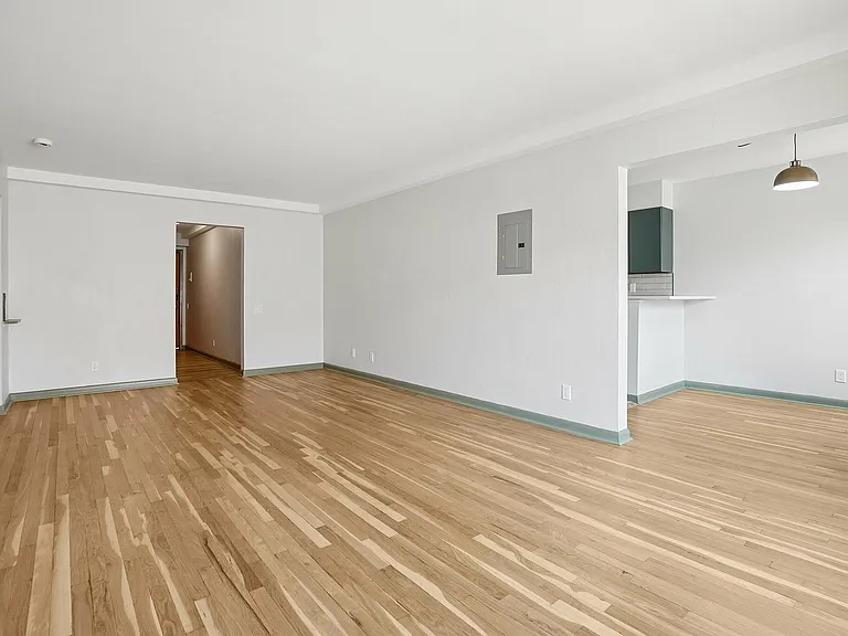 Spacious apartment with elegant hardwood floors and fresh white walls, featuring an open entryway and a cozy nook with overhead lighting.