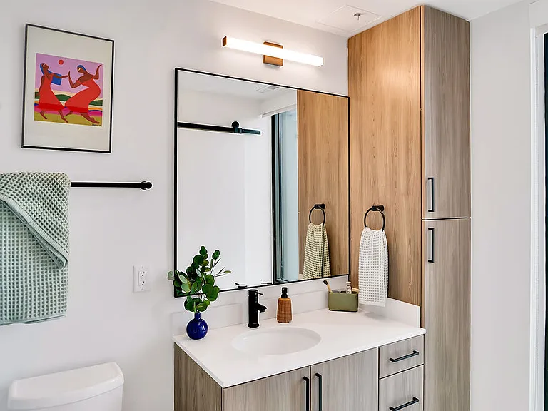 Modern bathroom with white walls, light wood cabinetry, large window, and decorative accents.