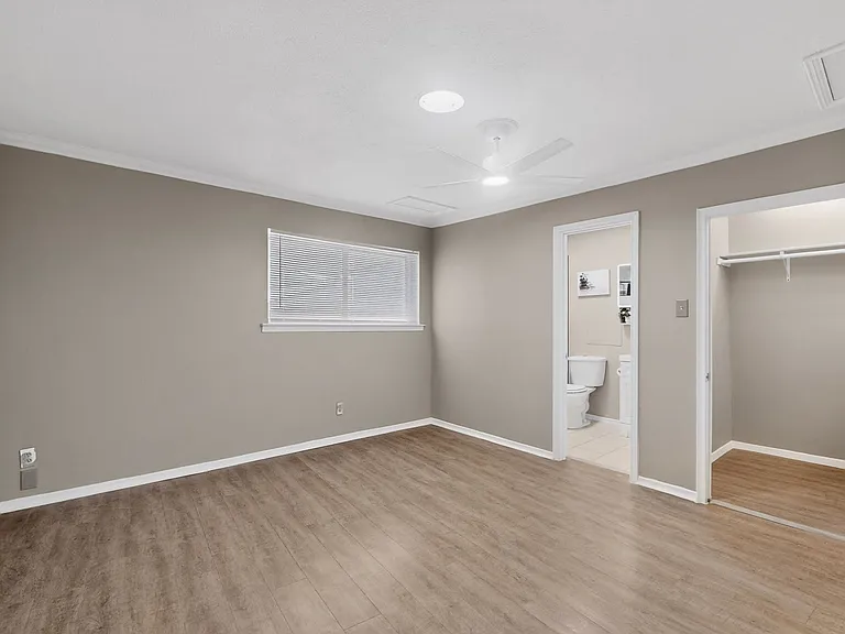 A spacious primary bedroom with wooden floors, a window, a ceiling fan, a walk-in closet and an en suite bath; designed for functionality and comfort.