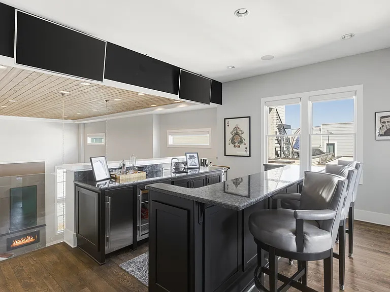 Upstairs mini bar conveniently located just steps from the rooftop patio and game room_perfect for mixing a drink before heading out. Two TVs located above the bar and a wine bottle shelf.