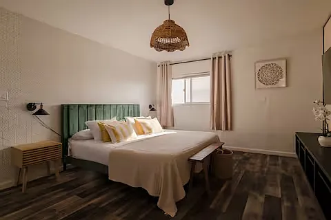 Bright, cozy master bedroom with a king-sized bed, green velvet headboard, soft bedding, natural light, and a crib, making it perfect for both parents and little ones.