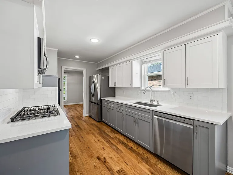 Kitchen featuring wood-finish flooring, white subway tile backsplash, white countertops, two-tone cabinetry, and stainless steel appliances