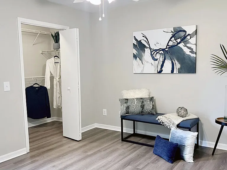 Experience the epitome of comfort in our signature master bedroom at Eagle's Pointe featuring sleek wood-style flooring, a spacious walk-in closet, and a convenient lighted ceiling fan.
