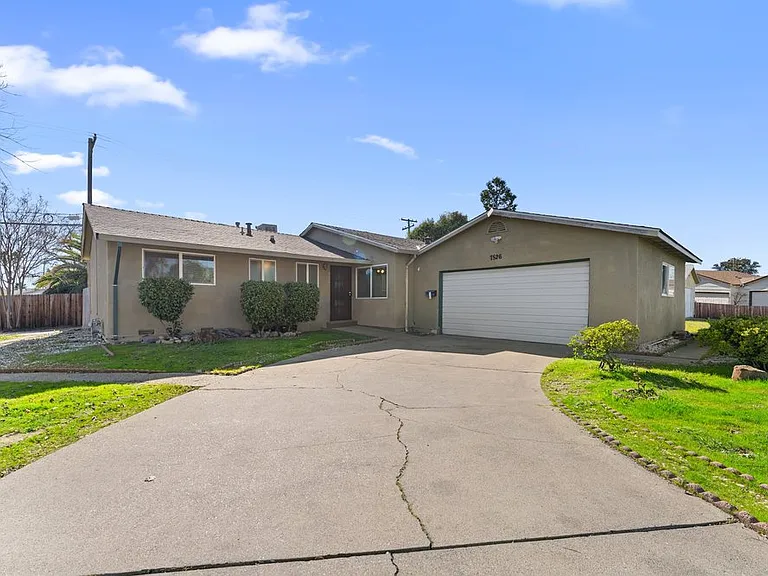 Charming front of home with extended driveway, lush greenery, and ample outdoor space.