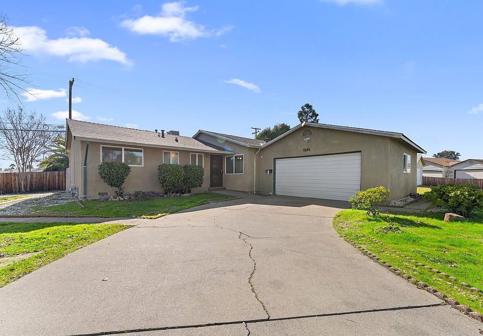 Charming front of home with extended driveway, lush greenery, and ample outdoor space.