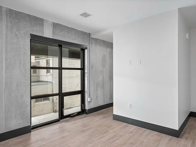 Modern industrial-style apartment with concrete walls, a large window, and sleek wooden flooring. Modern industrial-style apartment with concrete walls, a large window, and sleek wooden flooring.
