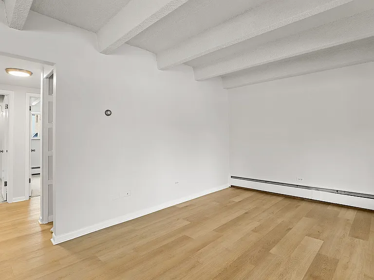 Bright and airy room with beautiful wood flooring, featuring modern minimalist design and exposed ceiling beams.