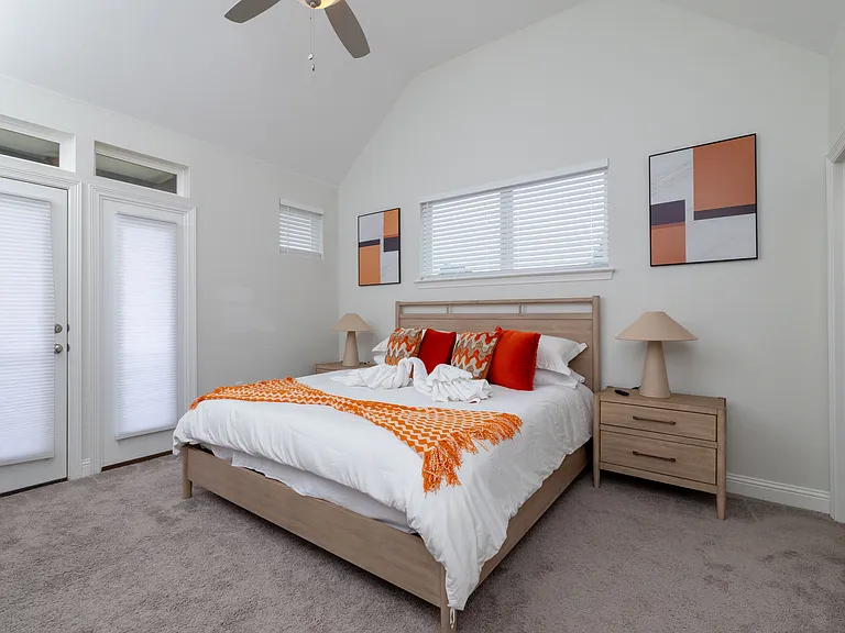 Primary bedroom features a king-size bed, corner chair, wall-mounted TV, backyard access, and an attached bathroom_your private retreat for comfort and relaxation.