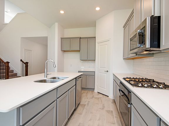 Well-equipped kitchen with quartz countertops, modern cabinetry, two sinks for added convenience, 4-burner gas stove, built-in microwave, dishwasher, and pantry access.