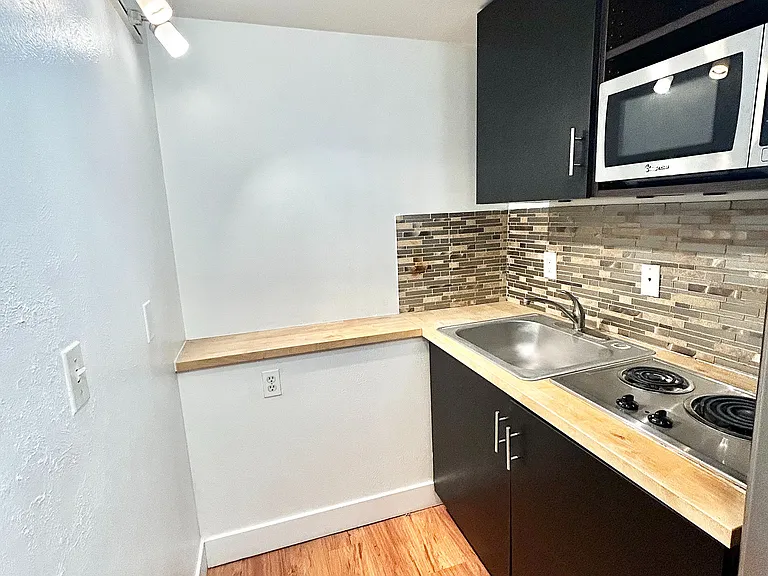 Chic kitchen nook featuring sleek black cabinets, modern appliances, and elegant wood flooring.