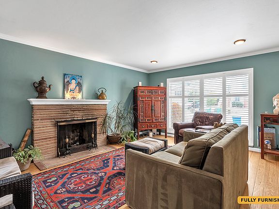Living room is set up with a TV, Sofa (pulls out to a full size bed), area rug, love seat, leather armchair and an ottoman as well as a shelf full of books.