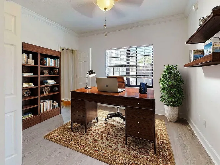 Elegant home office featuring a sophisticated wooden desk, built-in bookshelves, and stylish floating shelves with abundant natural light from a large window.