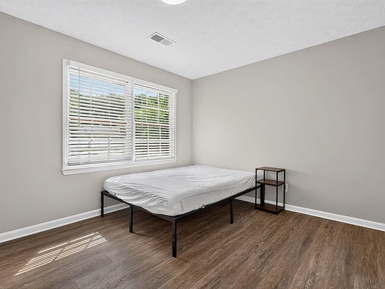 Private bedroom with large window, blinds, and durable wood-look flooring, offering space for a full bed and nightstand.