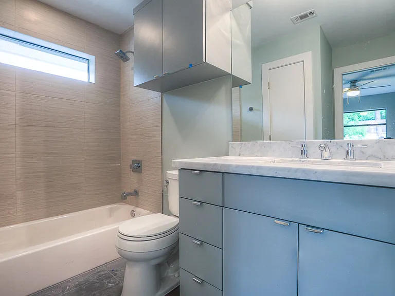 Modern guest bath with tile tub/shower surround, Carrara marble vanity, soft blue-gray cabinets, and a clerestory window for natural light