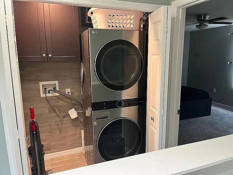 Bedroom hallway closet with washer/dryer, cabinets, and Dyson vacuum