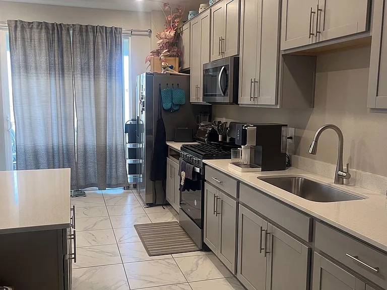 Galley-style kitchen with ample shaker cabinetry, stainless appliances, long counters, and a deep sink near patio doors.