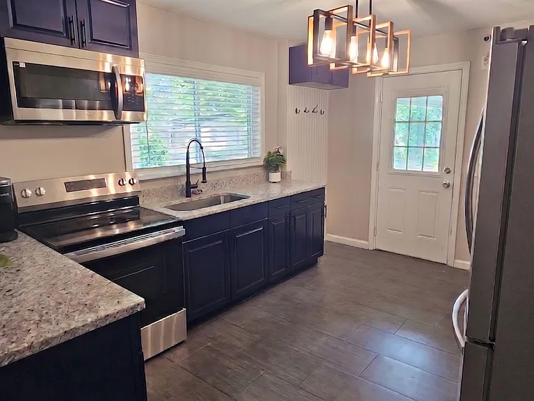 Galley kitchen with granite-look counters, stainless appliances, ample cabinetry, and a windowed sink plus back-door access.