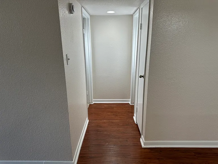 Bright hallway showcasing elegant wood-style flooring and sleek white trim, leading to bed and bathroom. Bright hallway showcasing elegant wood-style flooring and sleek white trim, leading to bed and bathroom.