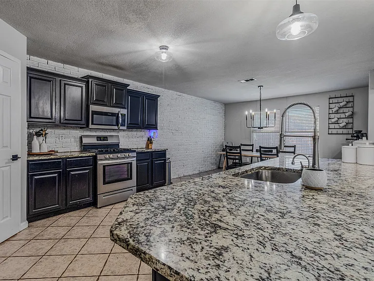 Kitchen featuring granite countertops, dark cabinetry, stainless steel appliances, and tile flooring