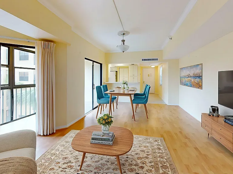 Bright and airy living space with cozy seating, elegant wood flooring, and contemporary dining area with turquoise chairs, enhanced by ample natural light from large windows.