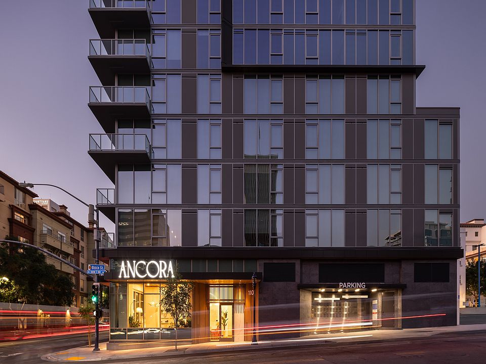 Elegant modern apartment building with glowing entrance, labeled Ancora, showcasing sleek architecture and ample parking.