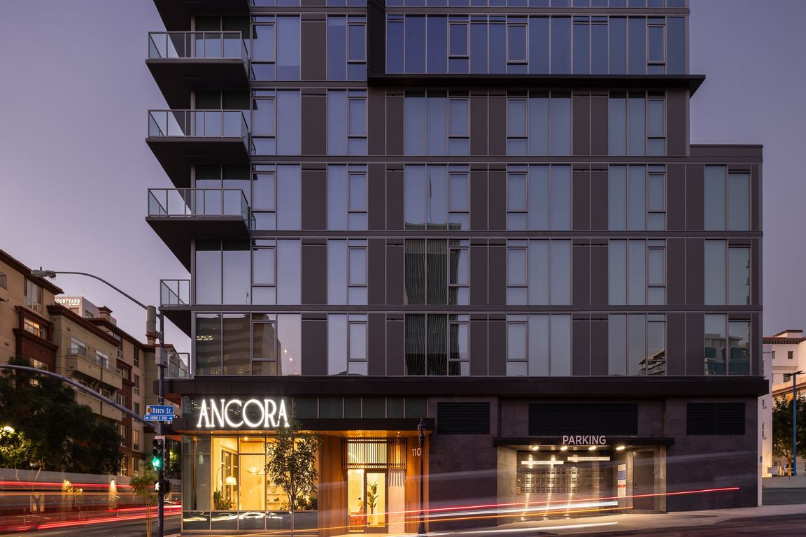 Elegant modern apartment building with glowing entrance, labeled Ancora, showcasing sleek architecture and ample parking.