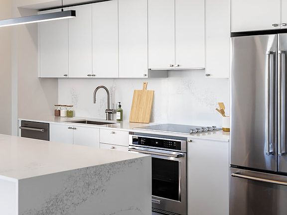 Signature Collection kitchen with white cabinetry, white marbled quartz countertop and backsplash, wine fridge, and upgraded stainless steel appliances