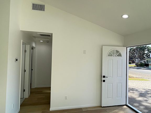 Light-filled living area with vaulted ceilings, recessed lighting, and welcoming front entry.