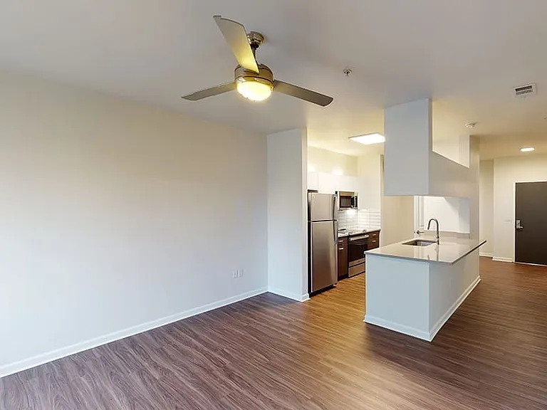 Apartment kitchen with stainless steel appliances, dining and living room with wood-style flooring.