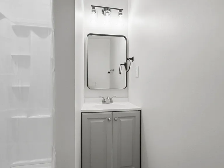 Bathroom vanity area with under-sink cabinet storage, framed mirror, updated lighting, and a tub/shower surround.