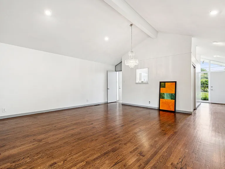 Expansive interior space featuring wood-finish flooring, vaulted ceilings, recessed lighting, a chandelier, and a white entry door with frosted sidelights