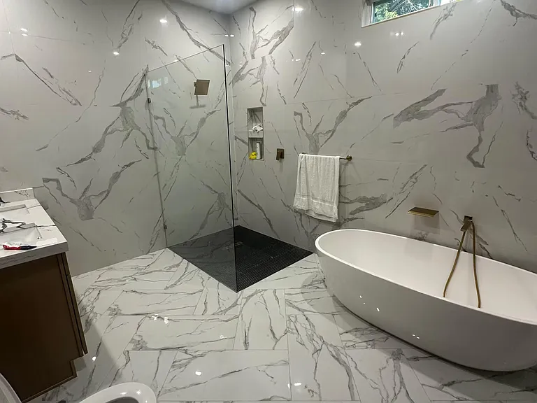 Spa-style bath with freestanding soaking tub, walk-in glass shower, and oversized marble-look tile throughout.