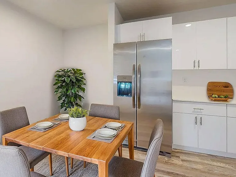 Modern kitchen and dining area featuring a sleek stainless steel refrigerator, elegant white cabinetry, and a stylish wooden dining table accented with greenery.