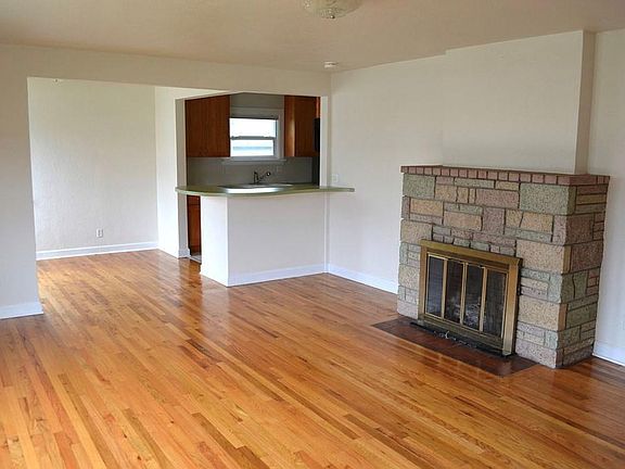 Living room looking east from entry. Small dining room to the left of kitchen. Fireplace burns wood. Floor is oak.
