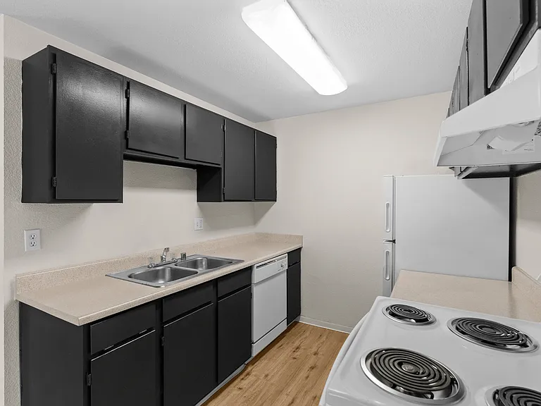 Kitchen with dark cabinetry, light countertops, double-basin sink, dishwasher, electric range, and full-size refrigerator at Garden Square Apartments in Lakewood, WA. Kitchen with dark cabinetry, light countertops, double-basin sink, dishwasher, electric 