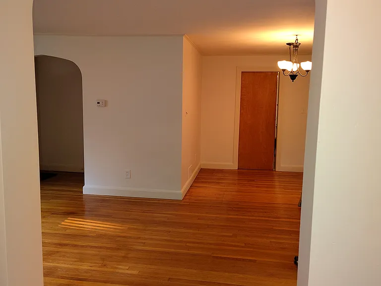 Showing the living/dining area from the hallway for the bedrooms. The door on the right is the pocket door to the kitchen, the archway to the left leads to the front door and front room.