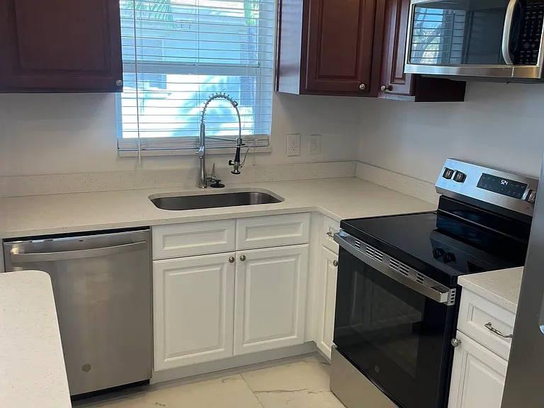 Newly renovated kitchen with white countertops and white cabinetry, commercial style stainless faucet, stainless appliances.
