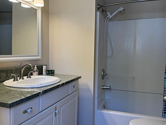Bathroom with marble counter top, bath shower combo, large linen closet, Kohler toilet and spacious cabinets beneath the vanity.
